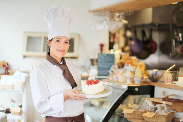 パン屋さんの店内でホールのショートケーキが乗ったお皿をもつ女性店員の写真