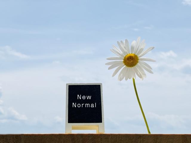 青空と花を背景に、「New Normal」と書かれたスタンド看板の画像