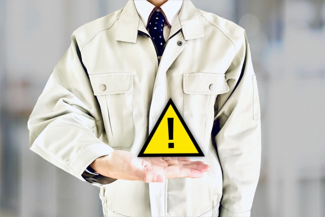 注意のアイコンを掌に出している、作業着を着た人の写真。