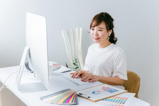 PCの前の笑顔の女性。デスクには色見表がある