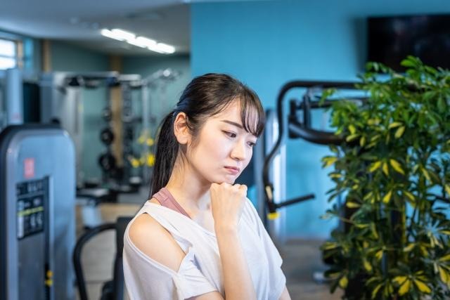 トレーニングジムの休憩スペースで悩んでいる女性の写真