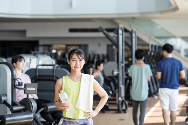 トレーニングジムを背景に、トレーニング終わりの女性が笑顔になっている写真